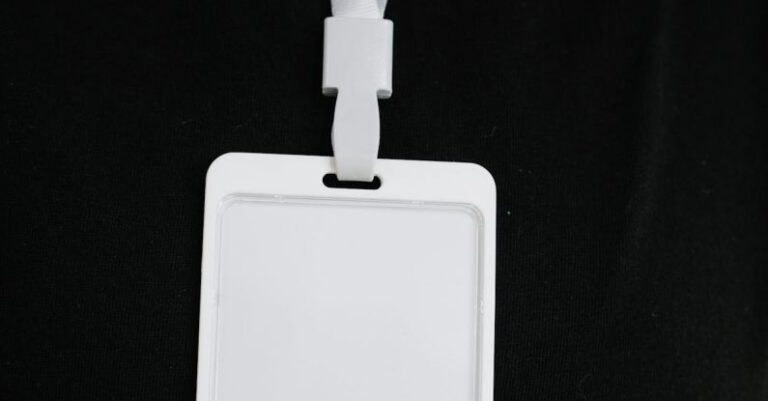 Guest Experiences - Plastic name tag with white ribbon and blank paper hanging on black background