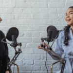 Hosting - Smiling African American female guest gesticulating while having interview with journalist sitting near mic