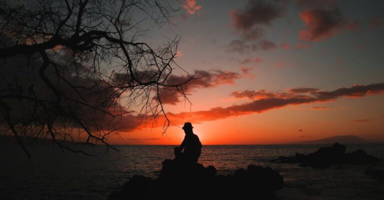 Ergonomic Seating - Silouhette of Person Seating on Stones Behind Body of Water